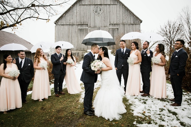 Winter wedding at pipers heath with couple standing in front of large barn with bridesmaids and groomsmen standing behind them