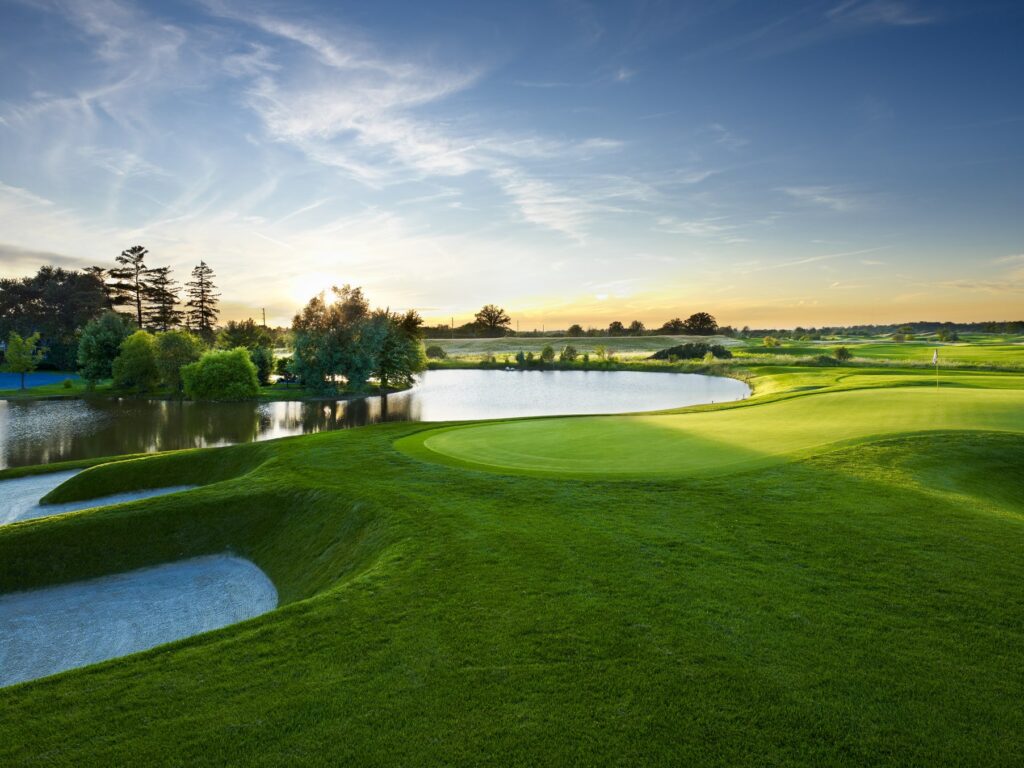 Golden hour image of Piper's Heath signature 14th hole from the entrance driveway with pond in the background